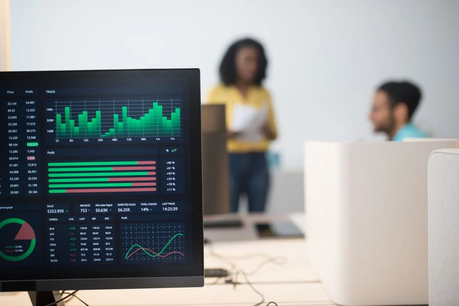 Hands using smartphone beside laptop with stock charts, showcasing digital trading.